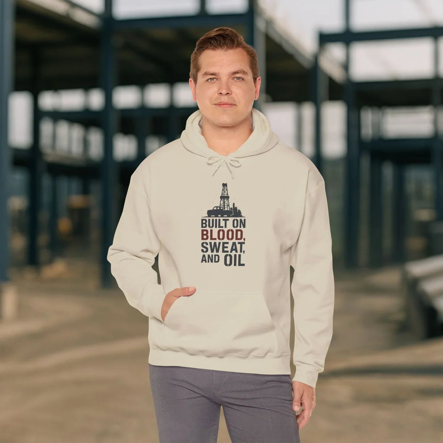 A person wearing a gray sweatshirt and maroon cap walks toward a lit oil rig at night. The sweatshirt reads “DON’T ASK MY ROUGHNECKS WHERE I NAP” in large maroon letters.