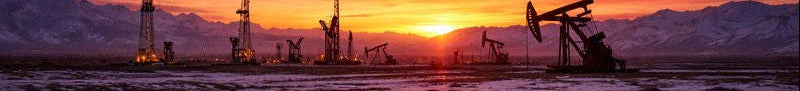 Oil pumpjacks operating in a field with a sunset sky and mountains in the background.